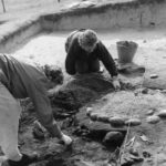 Excavating a pebble-lined open hearth in a Bronze Age roundhouse in 1960s